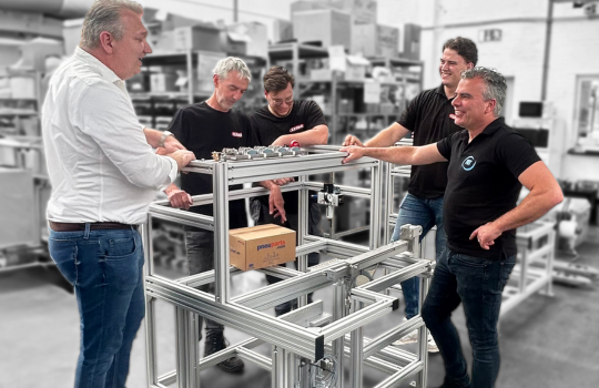 Employees Standing By the Frame Of A Machine